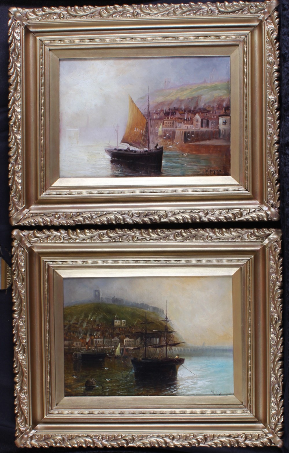 A matching pair of framed oil paintings depicting coastal harbour scenes with sailing vessels, set in ornate gold moulding.