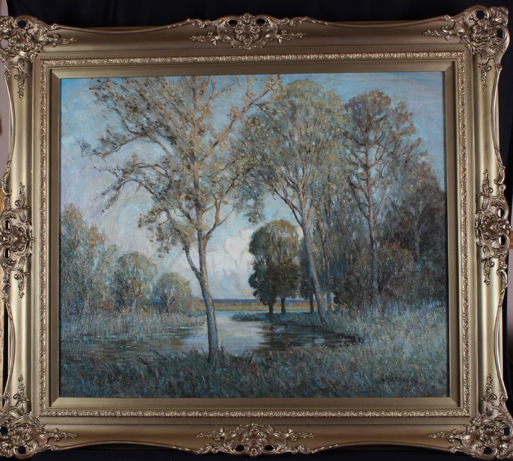 A large impressionistic oil painting depicting a calm lake surrounded by tall leafy trees, set within an ornate gilded frame.