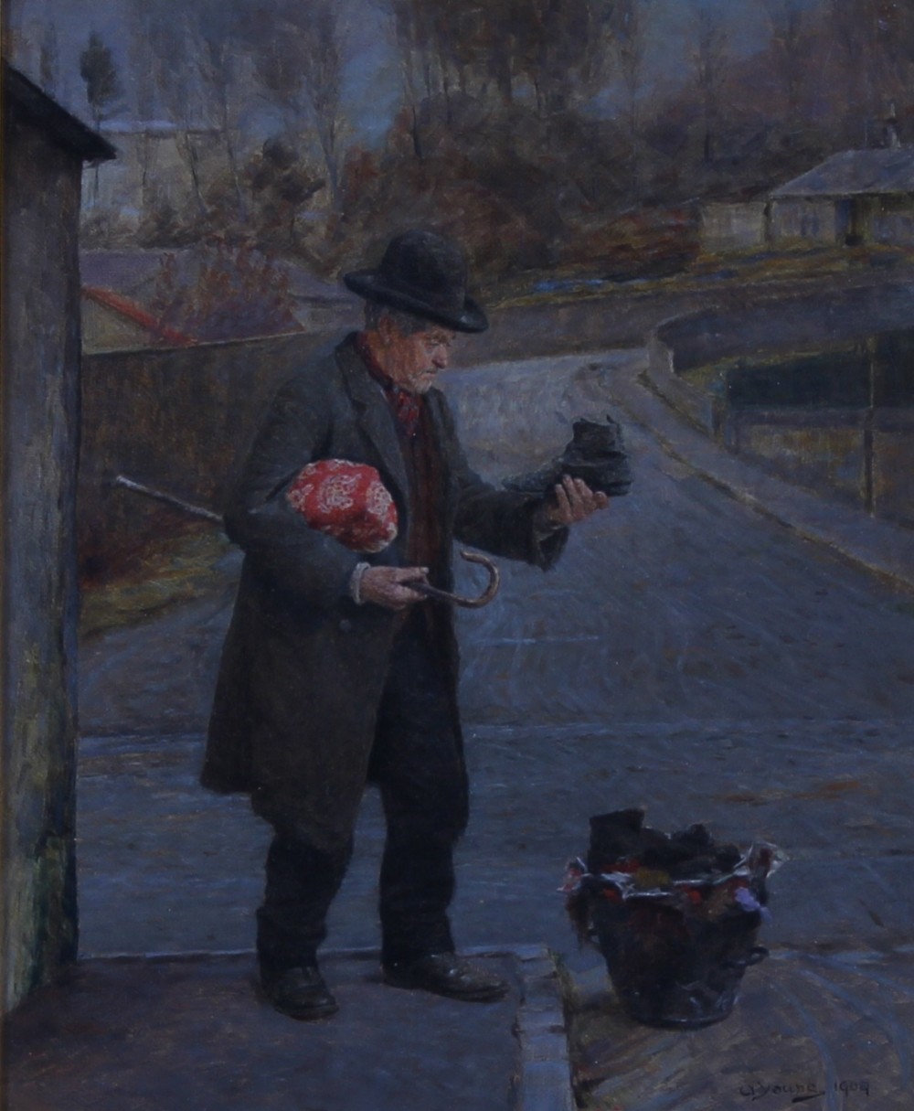 An Edwardian genre oil painting depicting a man standing on a paved village street examining a boot, rendered in muted blue and grey tones.