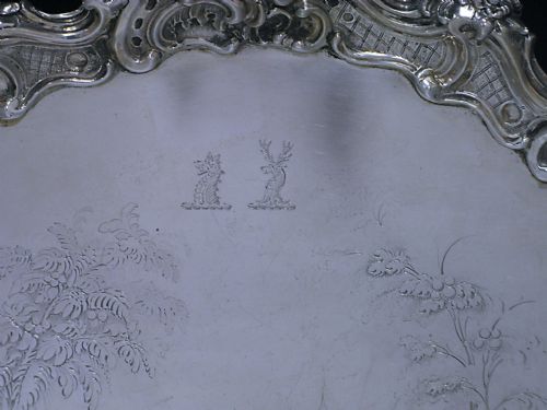 fig 1. A circular Victorian sterling silver salver featuring a moulded scroll and floral border around an engraved central landscape scene.