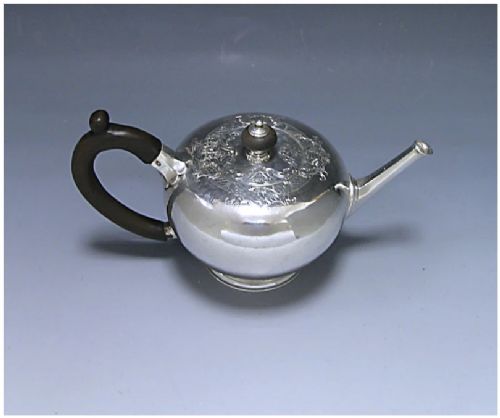 fig 1. A George II sterling silver bullet teapot featuring a spherical body, dark wooden handle, straight tapered spout, and a circular foot.