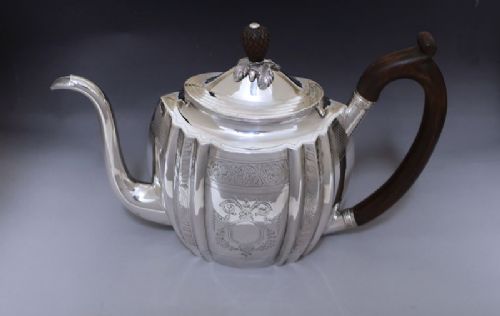 fig 1. A George III sterling silver teapot featuring bright-cut floral engraving, a lobed body, a carved wood handle, and a pinecone finial.