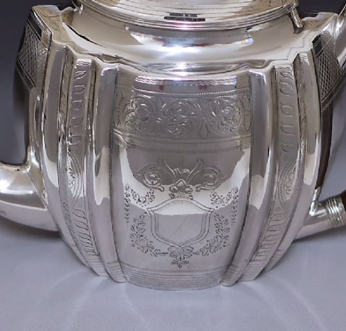 fig 2. A George III sterling silver teapot featuring bright-cut floral engraving, a lobed body, a carved wood handle, and a pinecone finial.