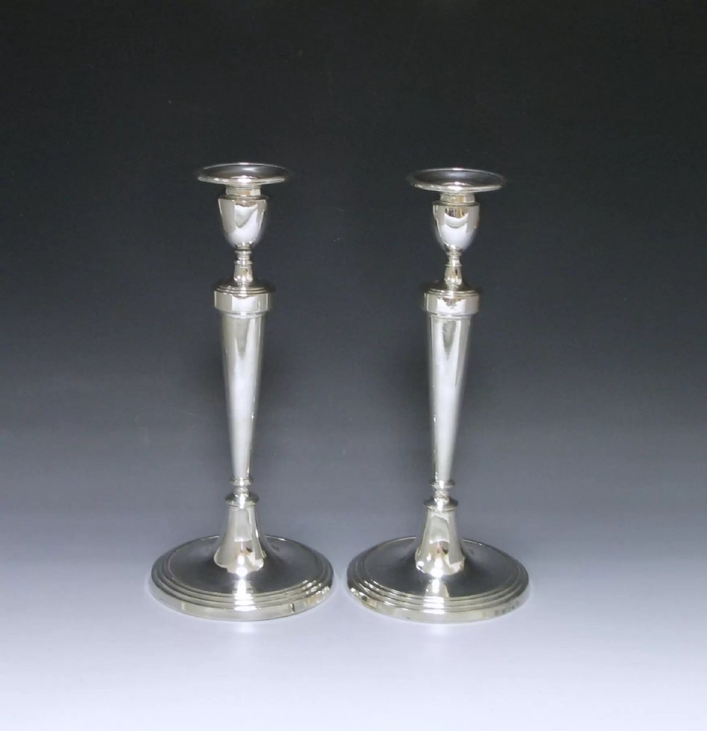 A pair of polished George III sterling silver candlesticks featuring tapered column shafts, urn sconces, and stepped circular bases.