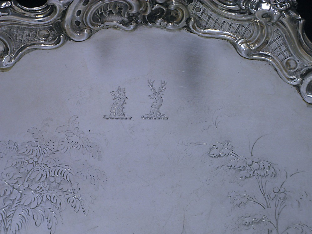 A circular Victorian sterling silver salver featuring a moulded scroll and floral border around an engraved central landscape scene. View II