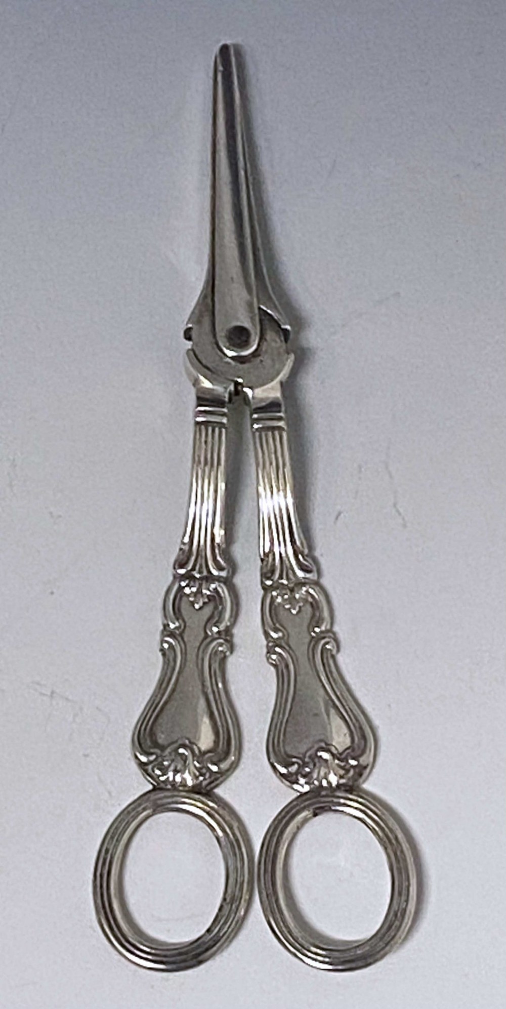 A pair of Victorian sterling silver grape scissors featuring Albert pattern handles with reeded finger loops.