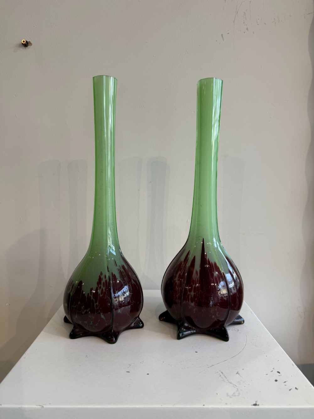A pair of tall French hand-blown art glass vases featuring slender green necks resting on bulbous burgundy spattered bases with pinched feet.
