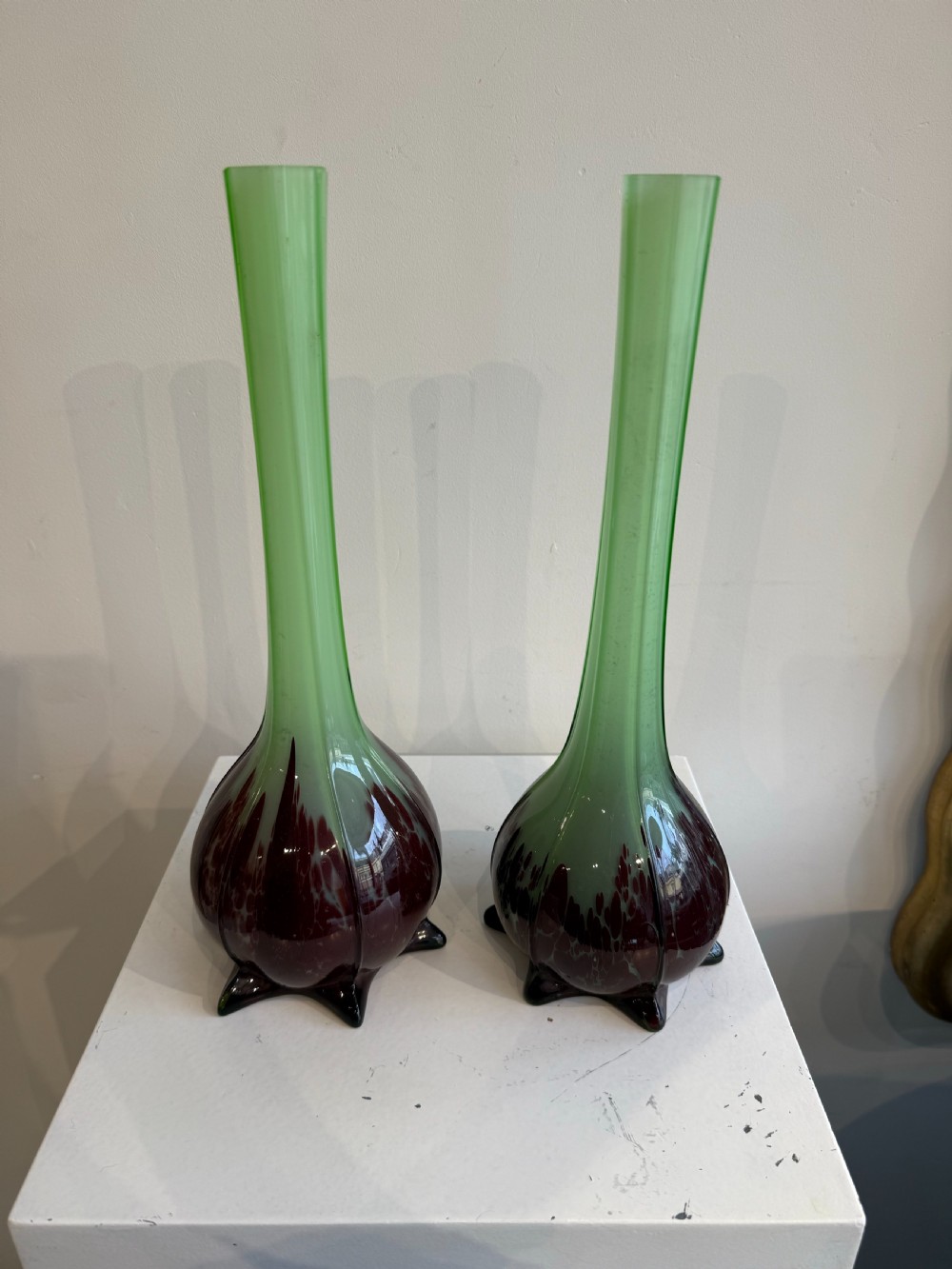A pair of tall French hand-blown art glass vases featuring slender green necks resting on bulbous burgundy spattered bases with pinched feet. View II