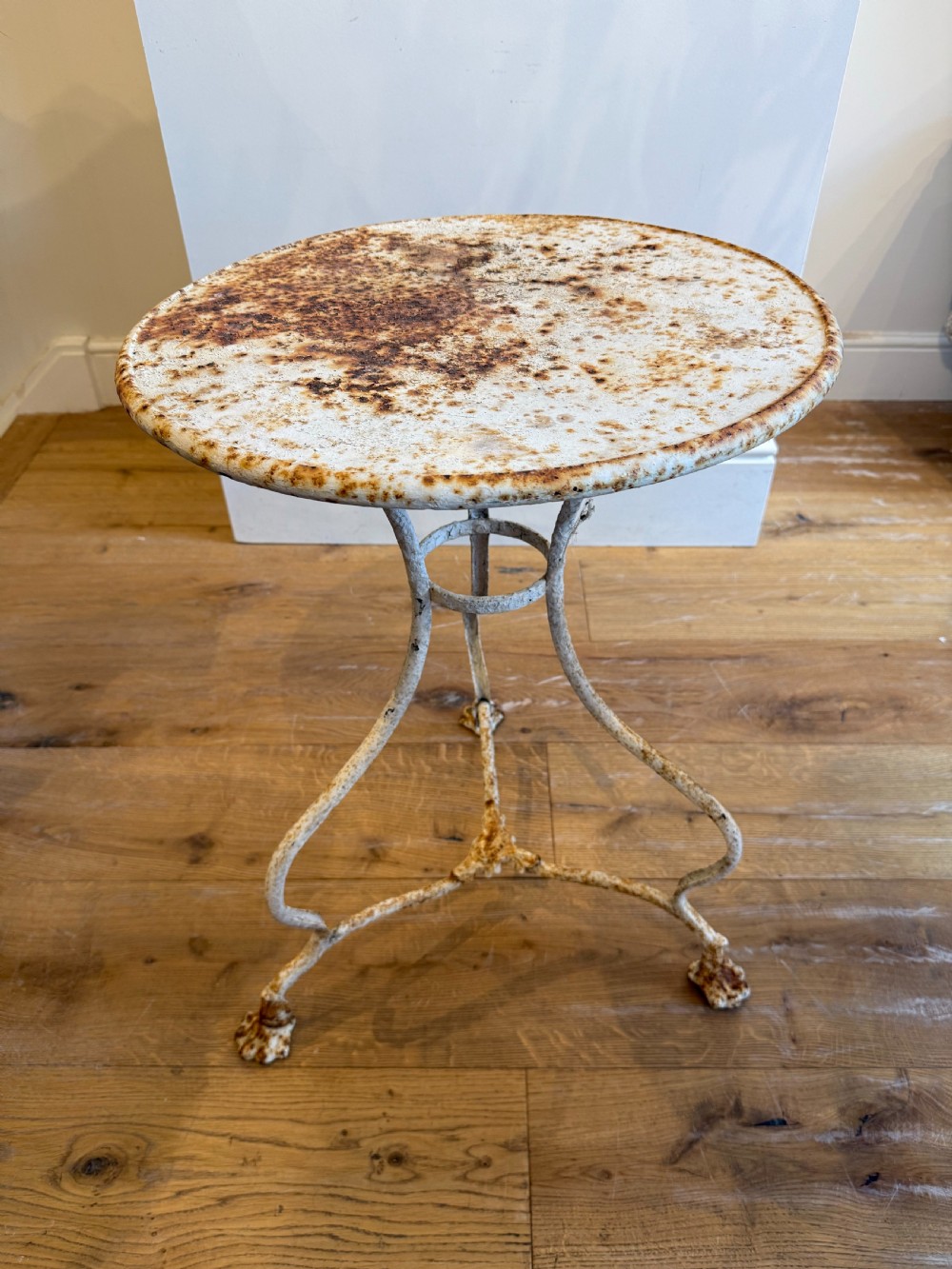 An antique round French Arras metal garden table with a weathered white painted finish, rust oxidisation, tripod legs, and signature claw feet.