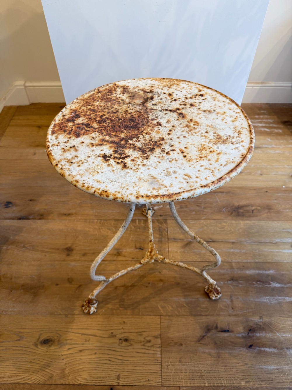 An antique round French Arras metal garden table with a weathered white painted finish, rust oxidisation, tripod legs, and signature claw feet. View II