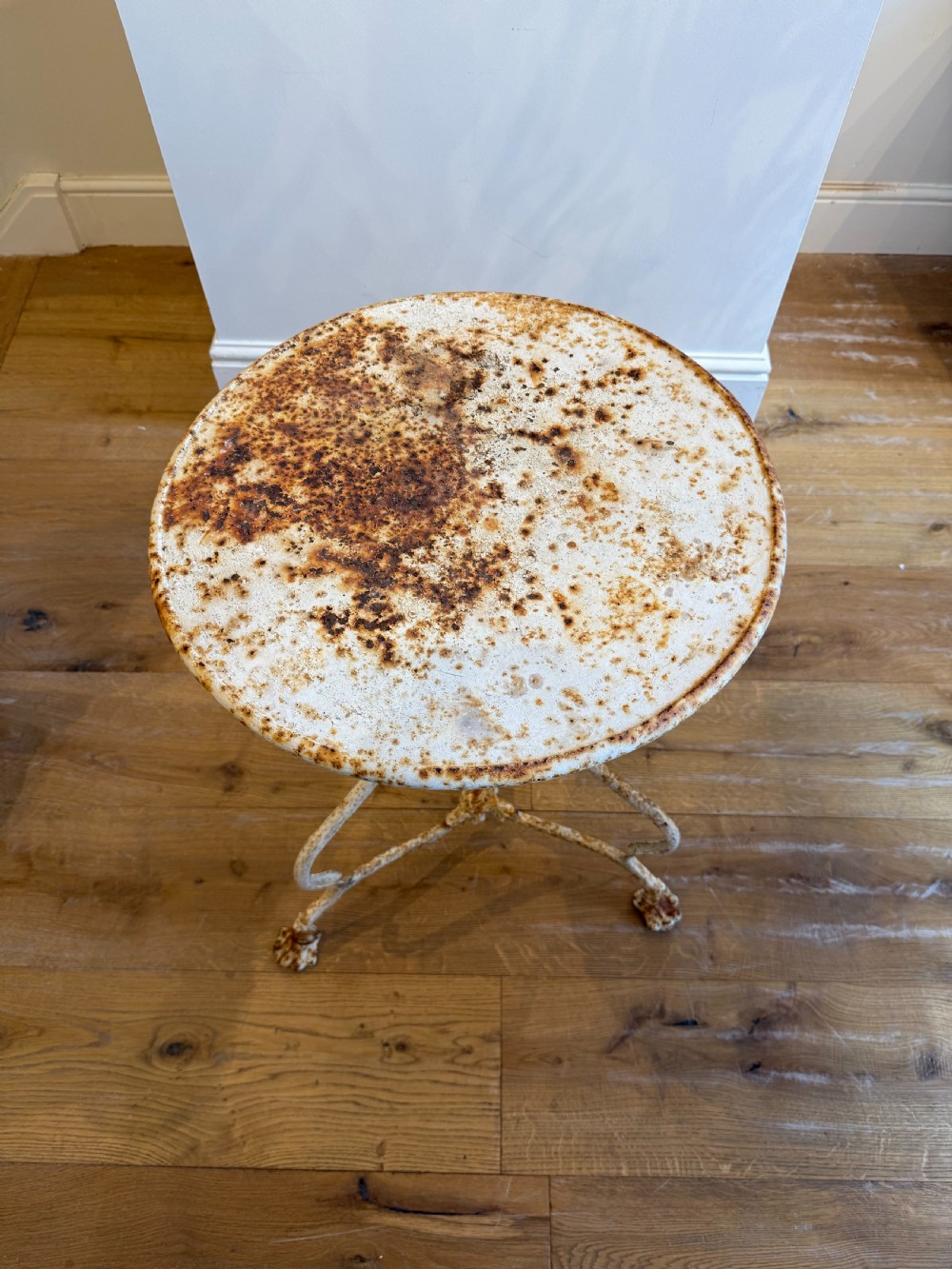 An antique round French Arras metal garden table with a weathered white painted finish, rust oxidisation, tripod legs, and signature claw feet. View III
