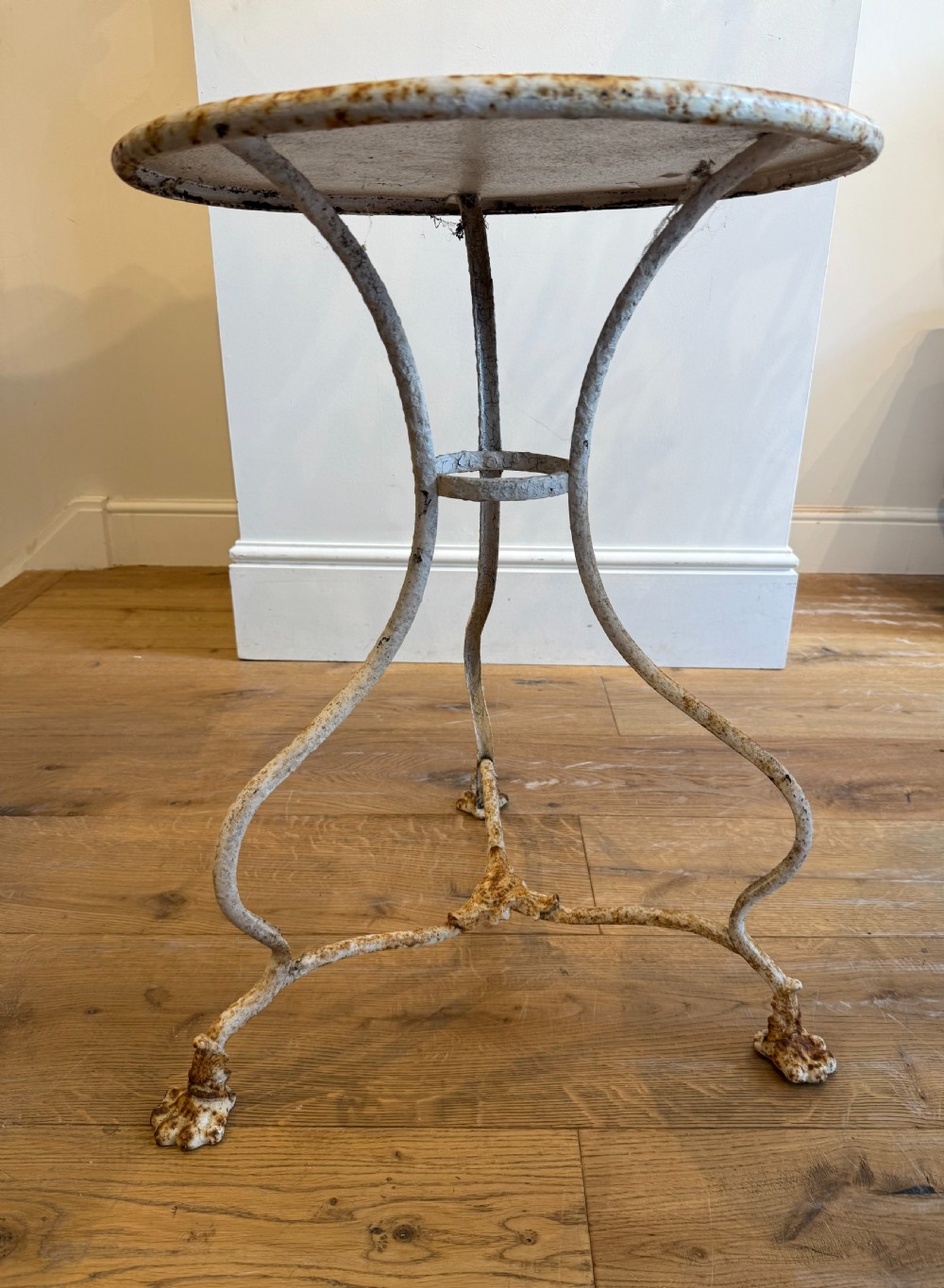 An antique round French Arras metal garden table with a weathered white painted finish, rust oxidisation, tripod legs, and signature claw feet. View IV