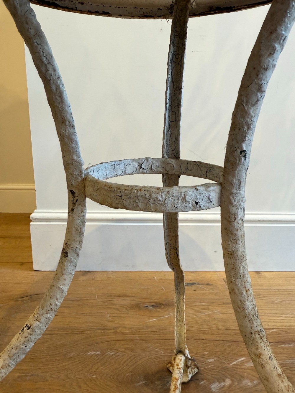 An antique round French Arras metal garden table with a weathered white painted finish, rust oxidisation, tripod legs, and signature claw feet. View IX