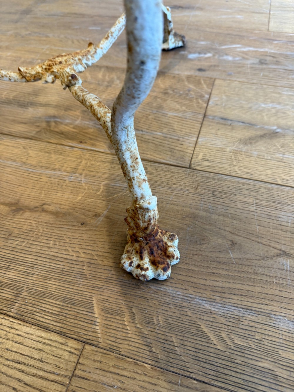 An antique round French Arras metal garden table with a weathered white painted finish, rust oxidisation, tripod legs, and signature claw feet. View X