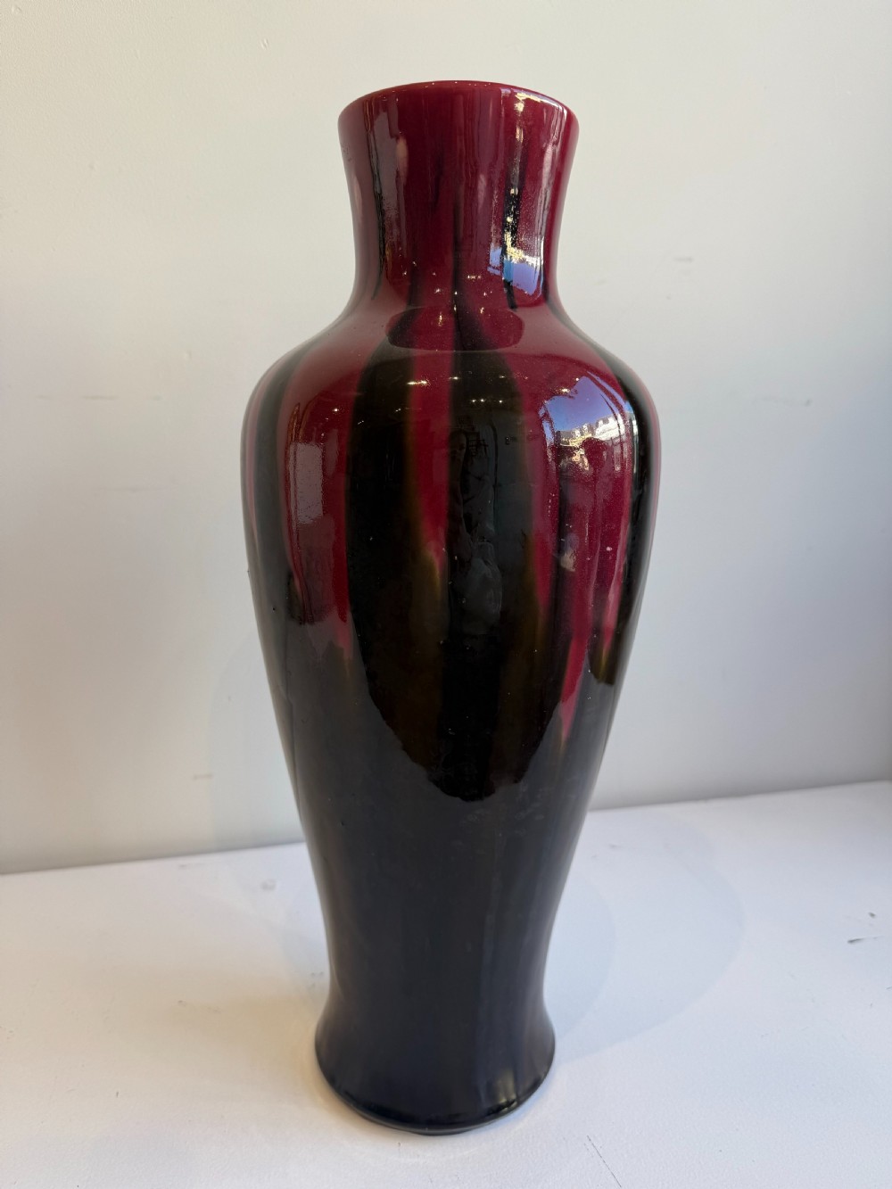 A tall, glossy ceramic baluster vase featuring a deep burgundy red glaze dripping over a dark brown and black body.