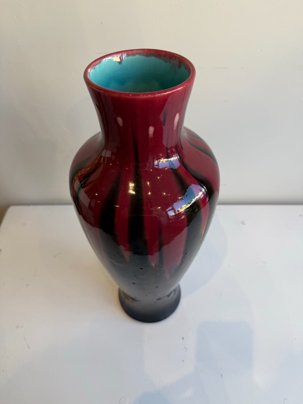 A tall, glossy ceramic baluster vase featuring a deep burgundy red glaze dripping over a dark brown and black body. View II