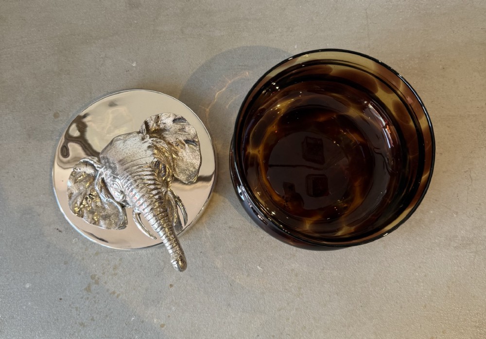 A circular faux tortoiseshell bowl with a polished silver-coloured metal lid featuring a sculpted elephant head in full relief. View V