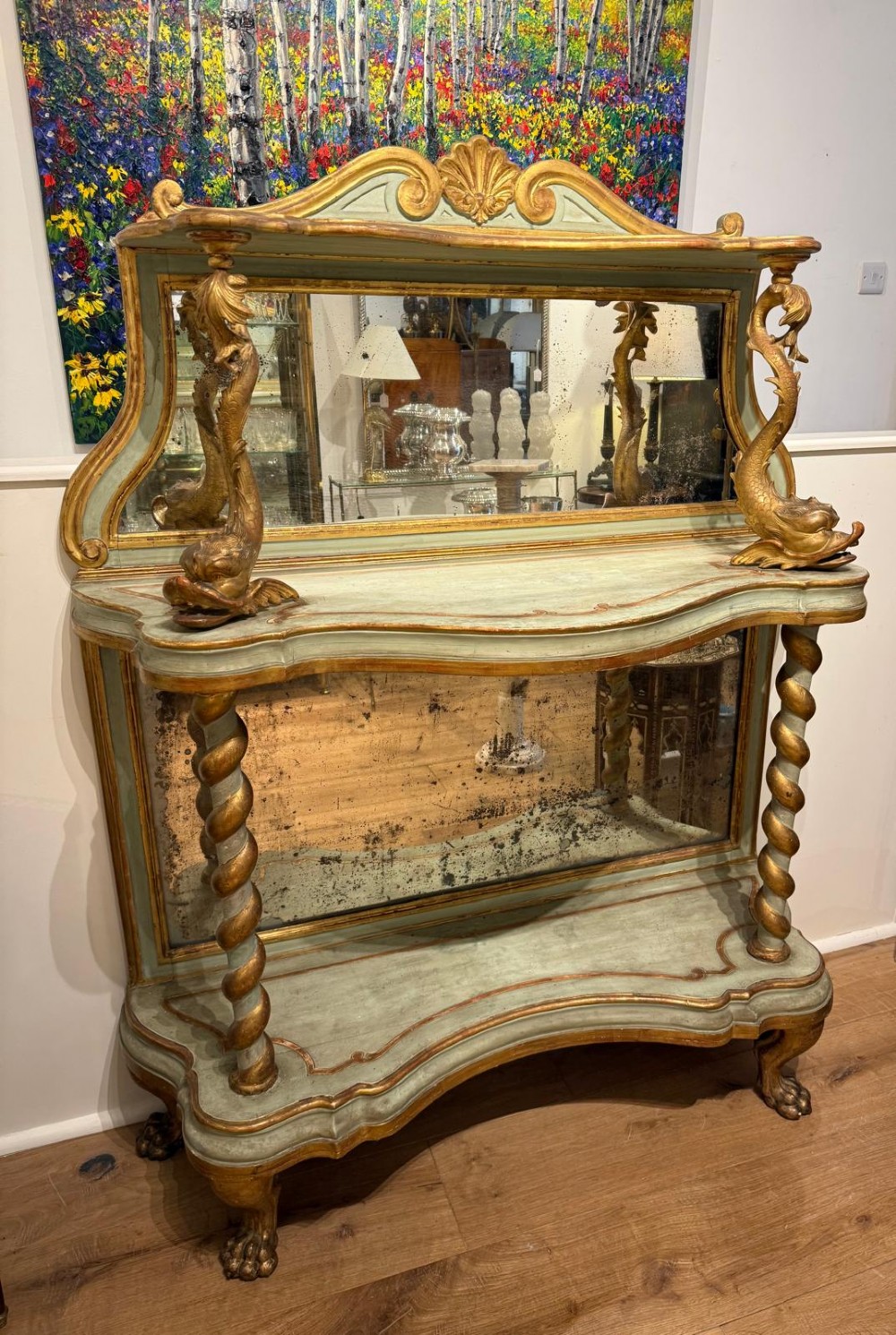 A Venetian Rococo style green painted and giltwood console table featuring carved dolphin supports, spiral columns, serpentine shelves, and mirrored back panels.