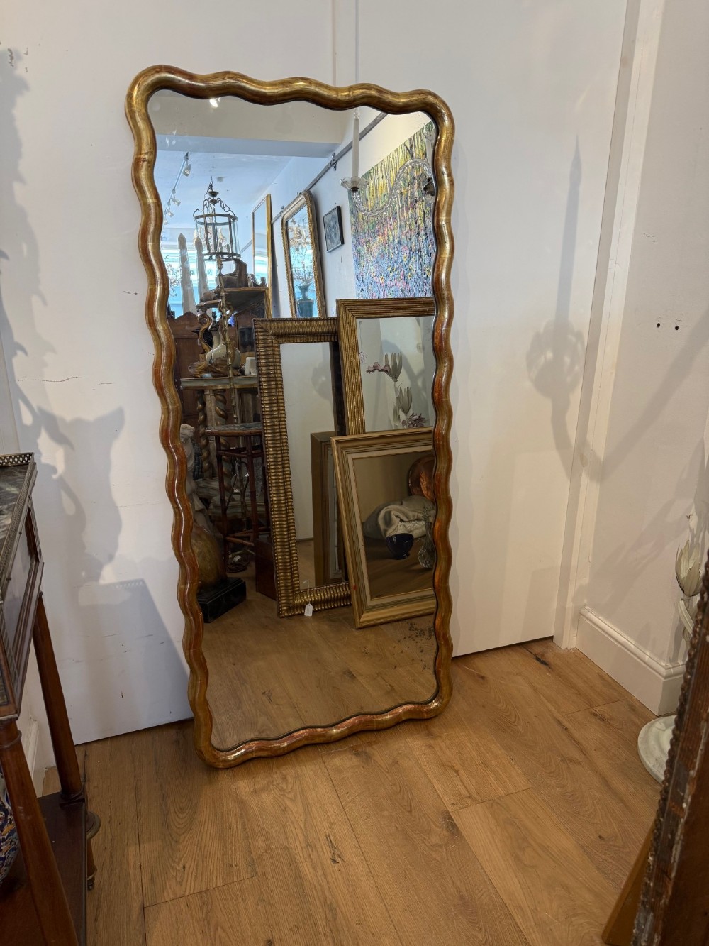 A tall full-length rectangular mirror featuring a gilded gold frame with a continuous wavy undulating edge.