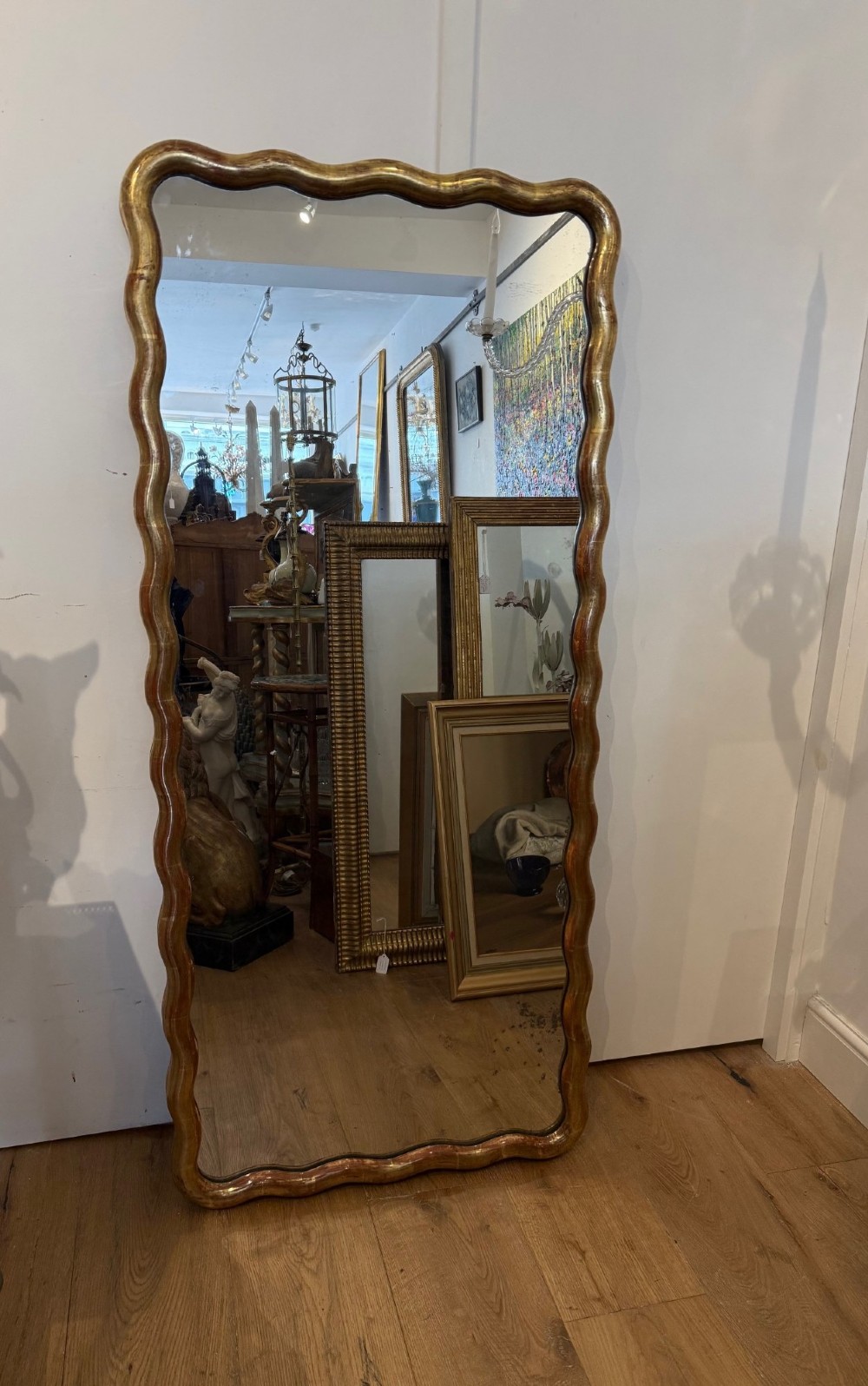 A tall full-length rectangular mirror featuring a gilded gold frame with a continuous wavy undulating edge. View II
