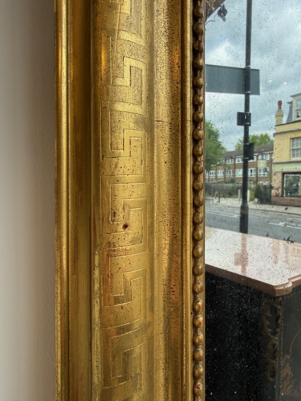 A large 19th-century French Louis Philippe mirror featuring a gilded frame with rounded upper corners, geometric relief moulding, beaded inner trim, and foxed mirror glass. View II