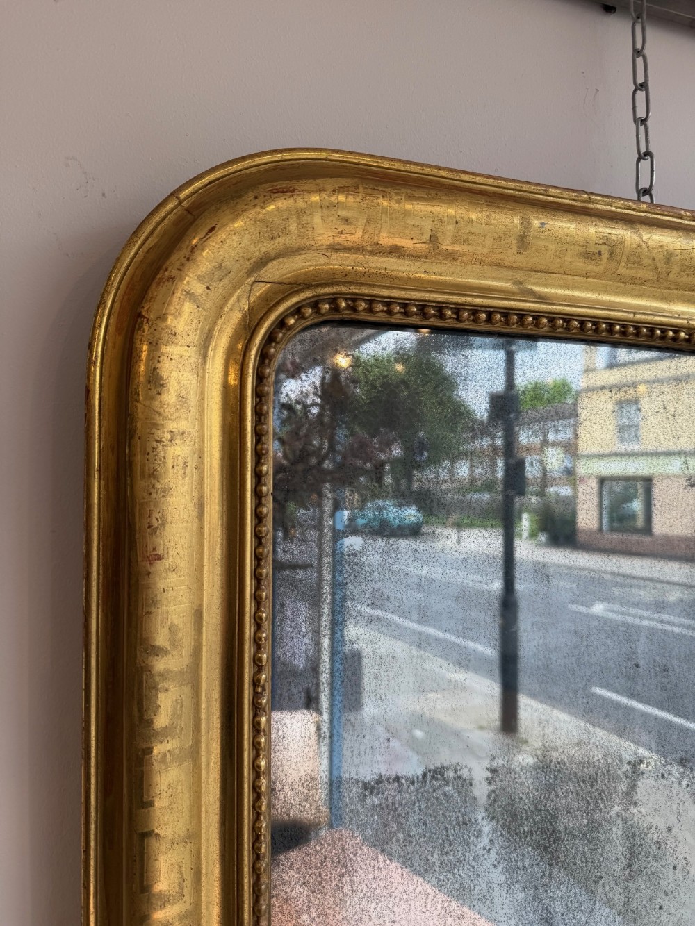A large 19th-century French Louis Philippe mirror featuring a gilded frame with rounded upper corners, geometric relief moulding, beaded inner trim, and foxed mirror glass. View VI