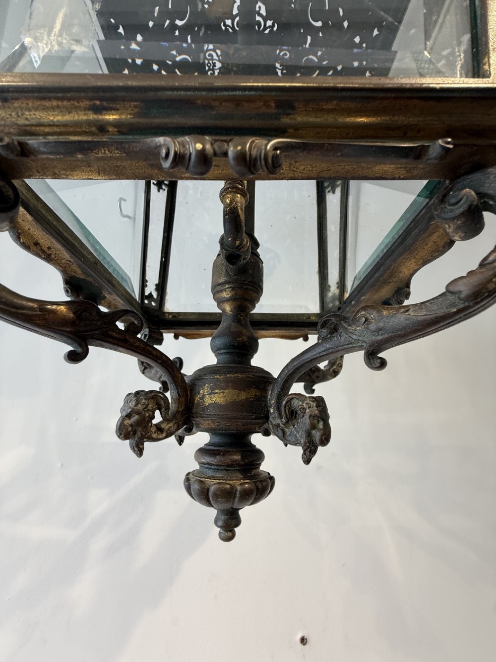 An antique patinated bronze hanging hall lantern featuring clear glass panels, ornate pierced metal cresting, and a scrolled lower finial. View VIII