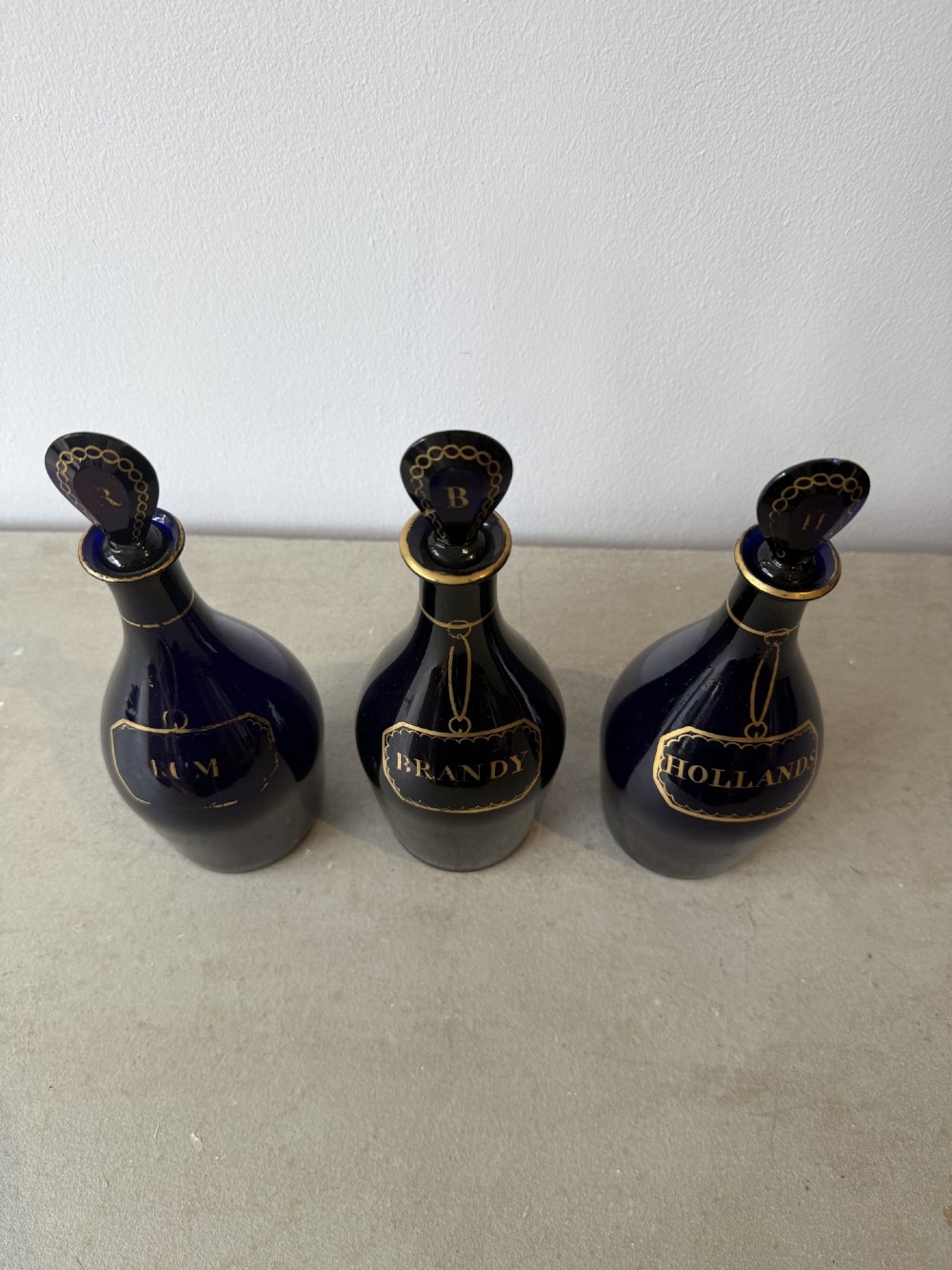 A set of three cobalt blue glass decanters with gilded labels for Brandy, Hollands, and Rum, complete with matching initialled stoppers. View II