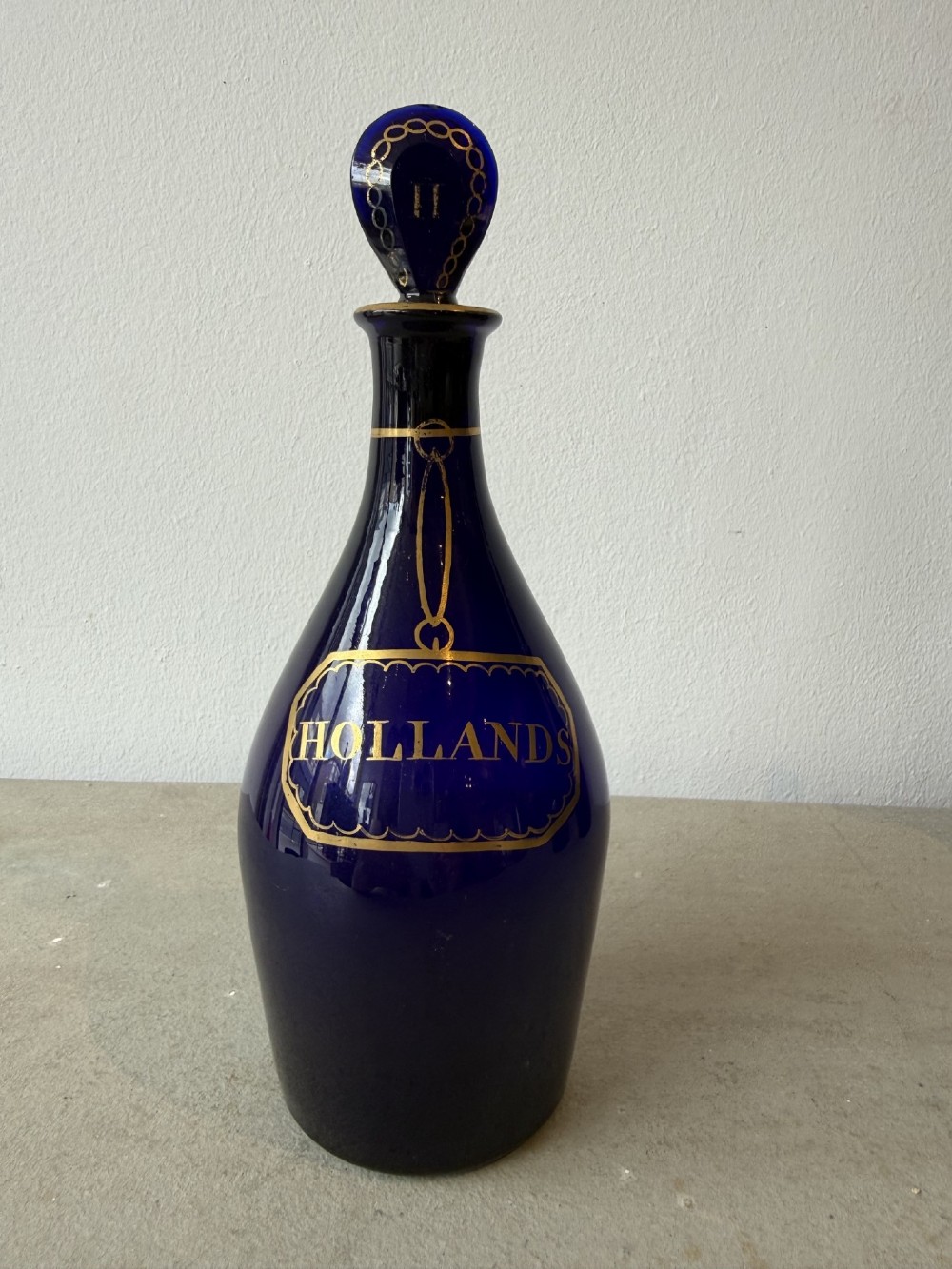 A set of three cobalt blue glass decanters with gilded labels for Brandy, Hollands, and Rum, complete with matching initialled stoppers. View V