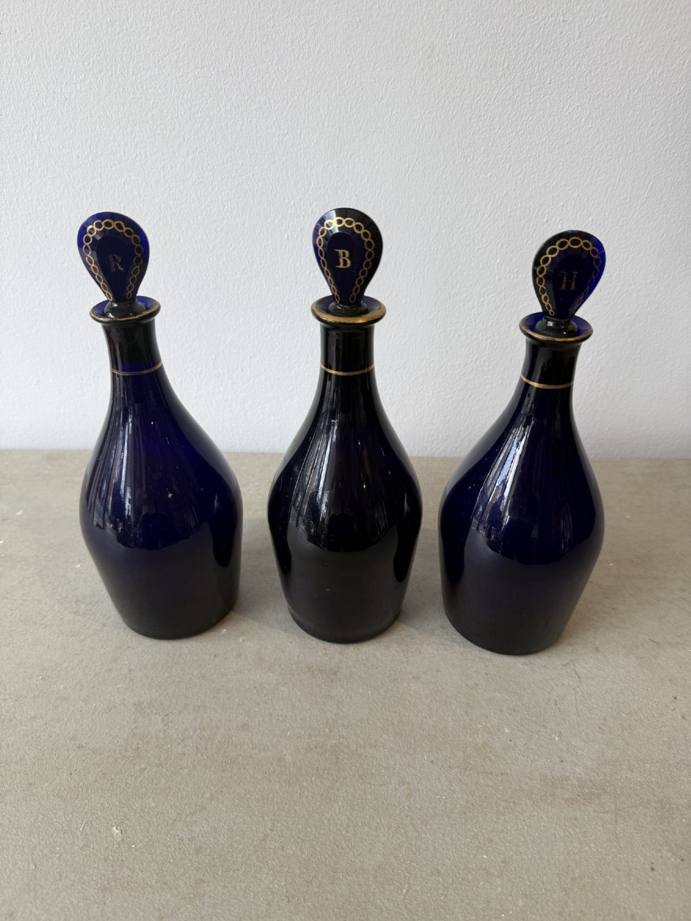 A set of three cobalt blue glass decanters with gilded labels for Brandy, Hollands, and Rum, complete with matching initialled stoppers. View VI