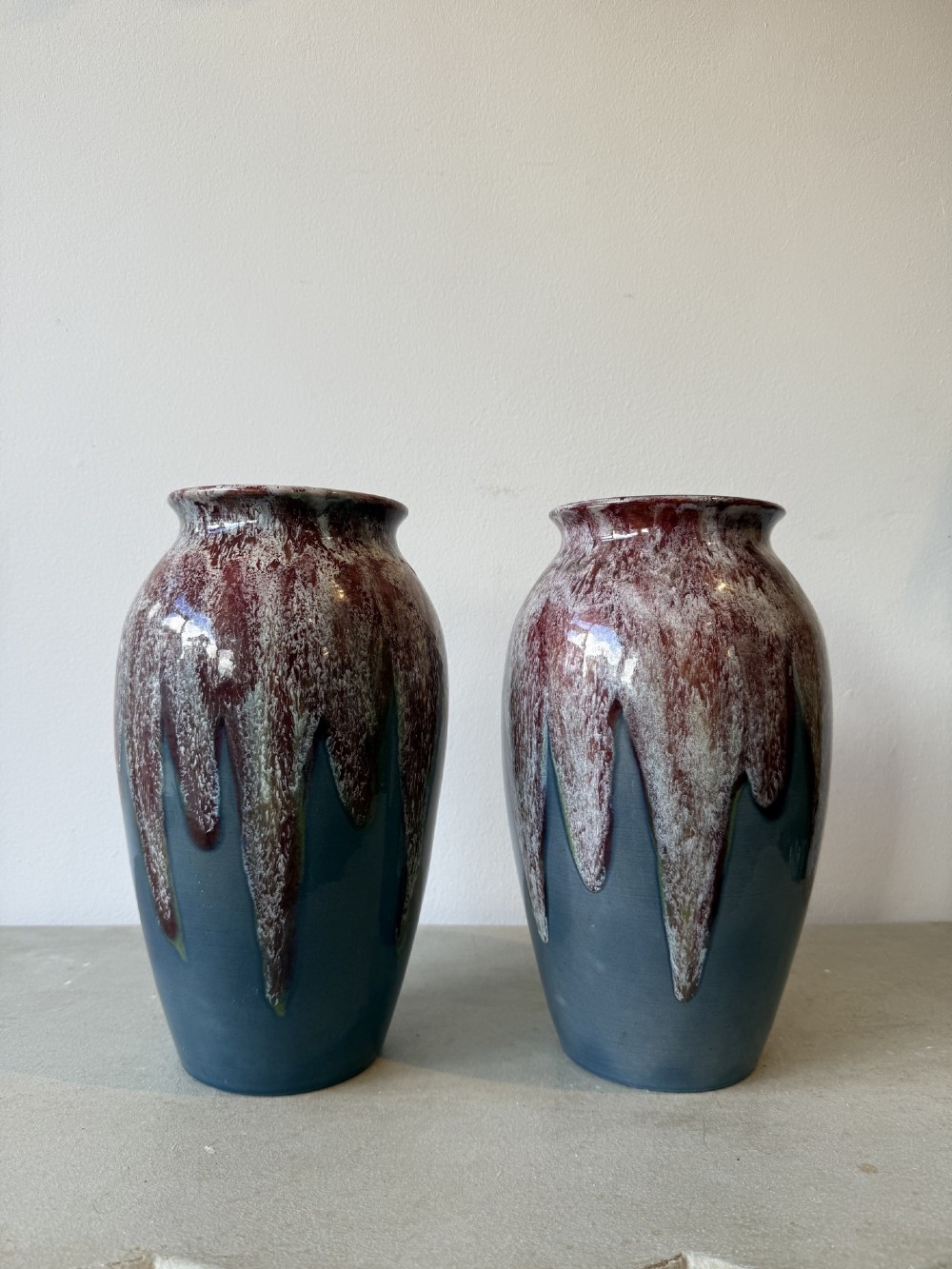 A pair of glazed ceramic art pottery vases featuring a running burgundy and white speckled drip glaze over a matte slate blue base.