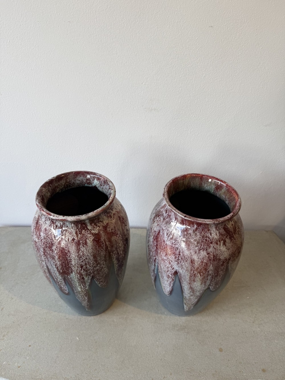 A pair of glazed ceramic art pottery vases featuring a running burgundy and white speckled drip glaze over a matte slate blue base. View II