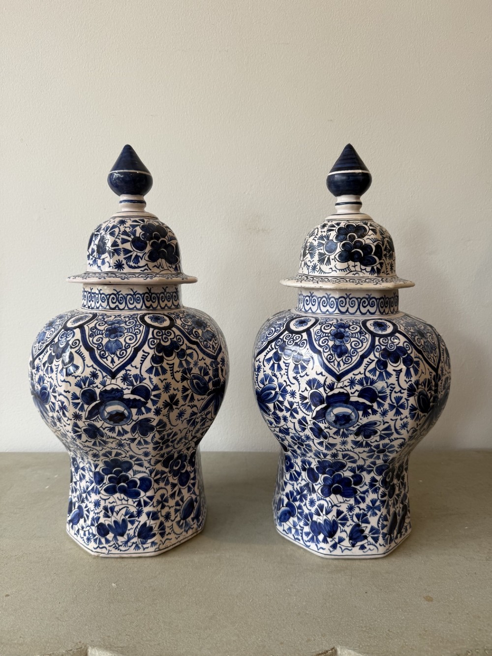 A pair of octagonal tin-glazed earthenware lidded vases decorated with hand-painted blue floral patterns on a white ground, topped with pointed finials.