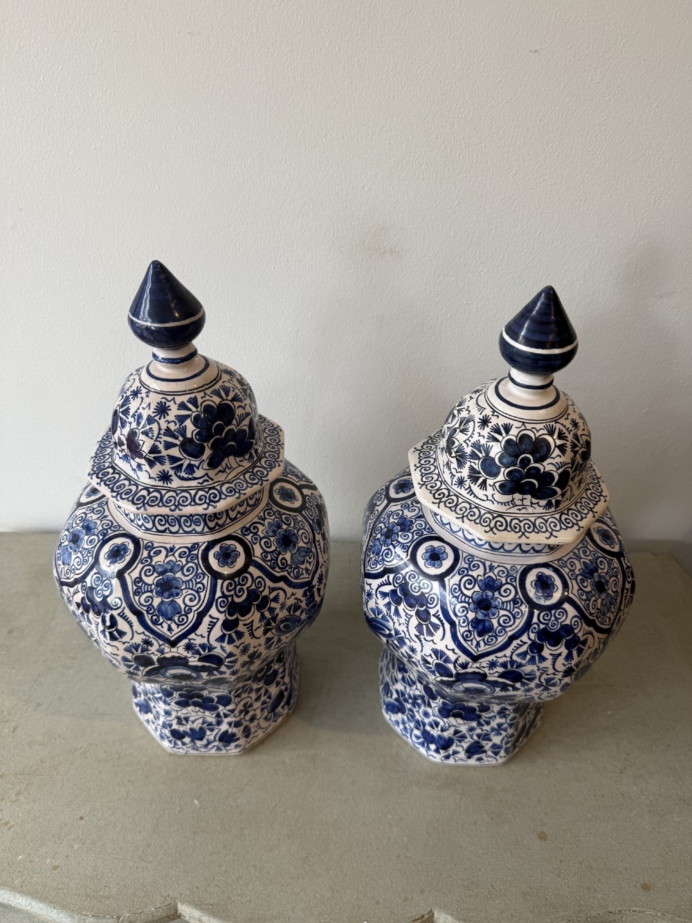 A pair of octagonal tin-glazed earthenware lidded vases decorated with hand-painted blue floral patterns on a white ground, topped with pointed finials. View II