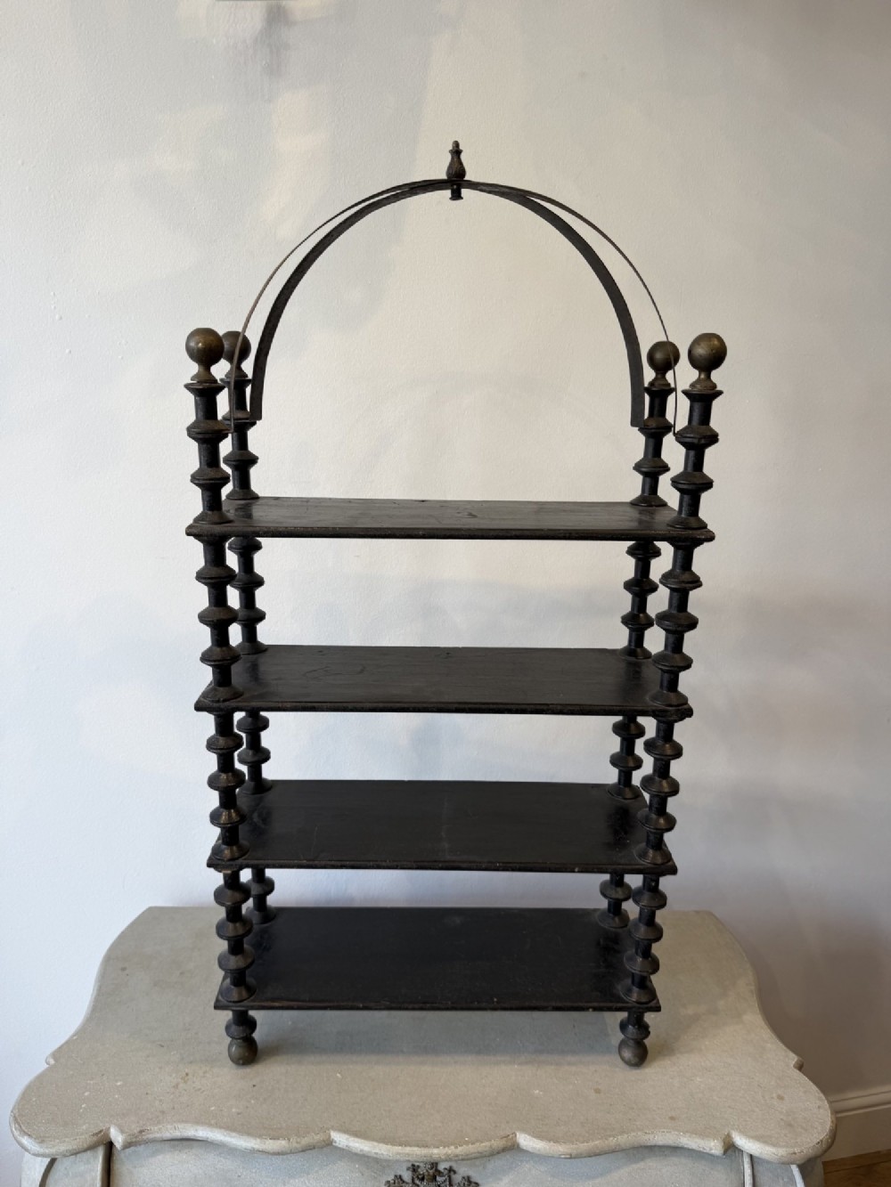 A four-tiered ebonised black wooden display shelf featuring bobbin-turned corner supports, top finials, and an arched metal top handle.