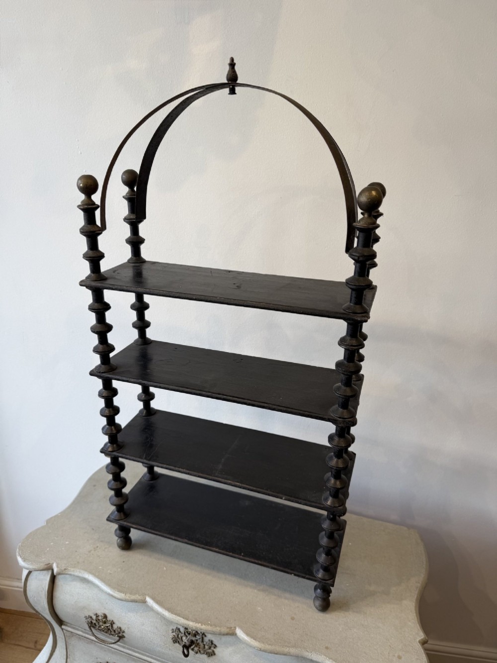 A four-tiered ebonised black wooden display shelf featuring bobbin-turned corner supports, top finials, and an arched metal top handle. View II