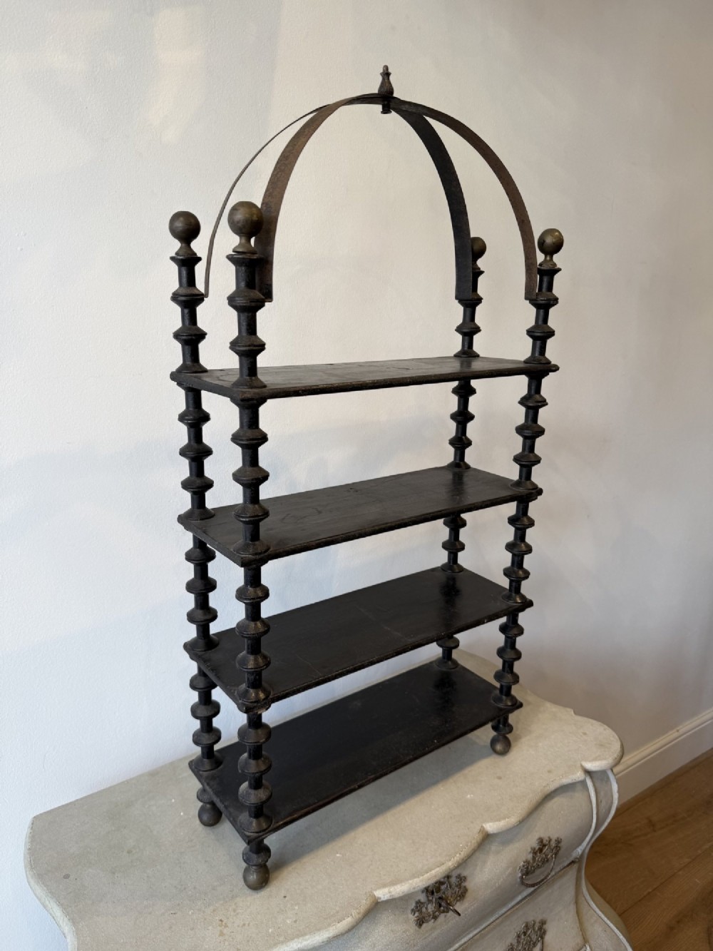 A four-tiered ebonised black wooden display shelf featuring bobbin-turned corner supports, top finials, and an arched metal top handle. View III