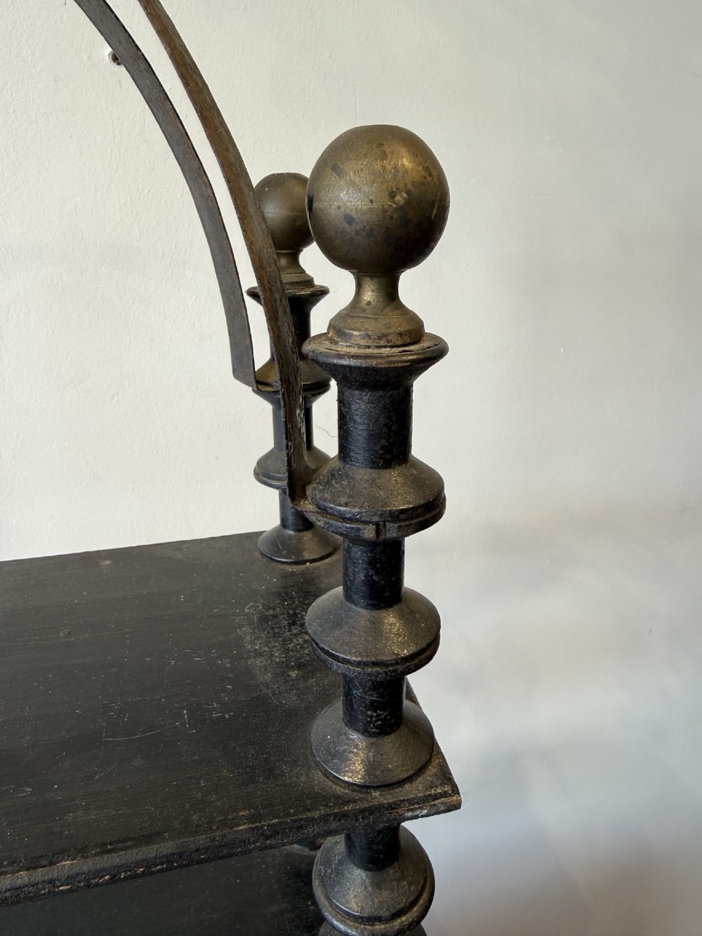 A four-tiered ebonised black wooden display shelf featuring bobbin-turned corner supports, top finials, and an arched metal top handle. View IV