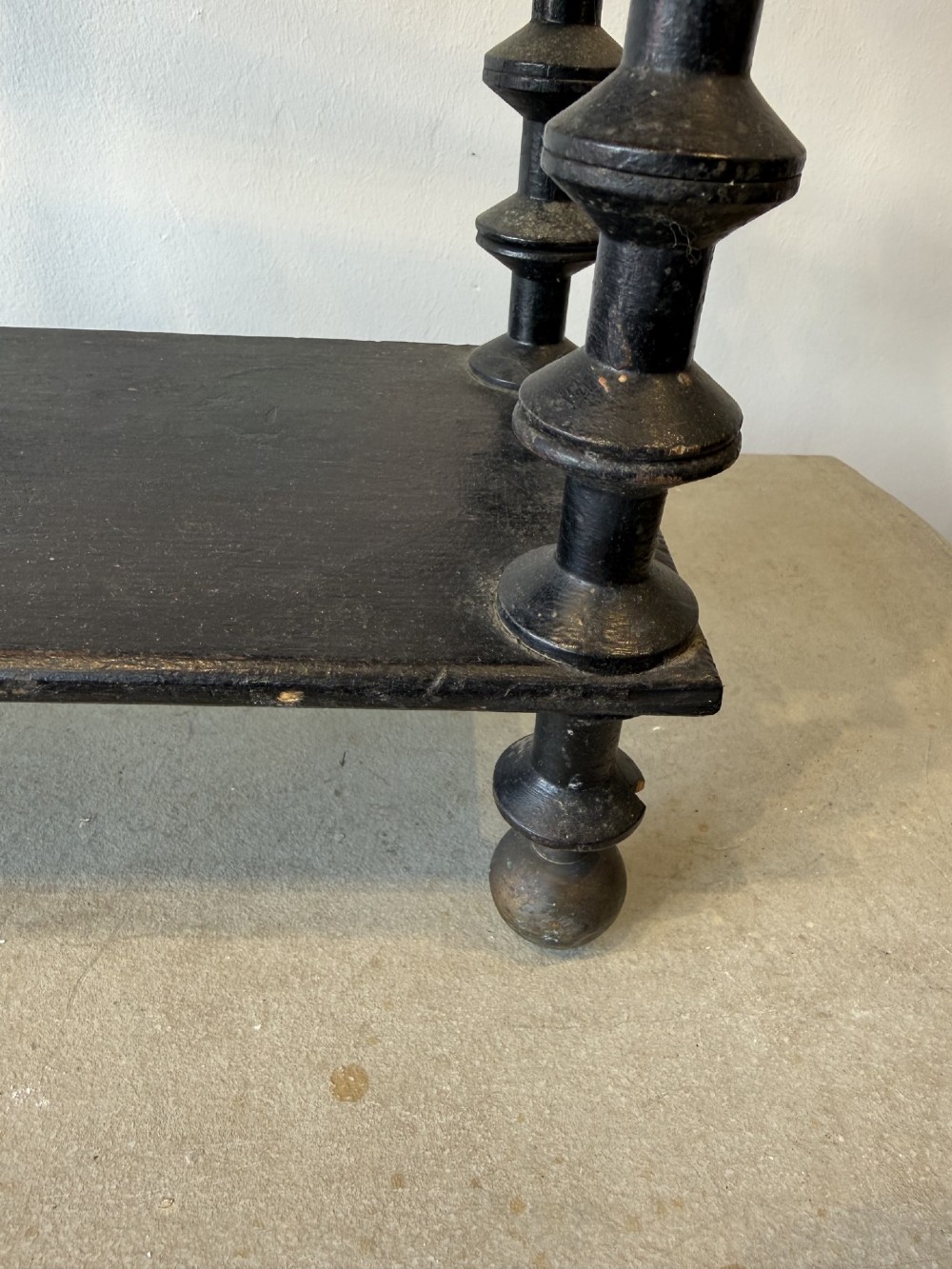 A four-tiered ebonised black wooden display shelf featuring bobbin-turned corner supports, top finials, and an arched metal top handle. View V