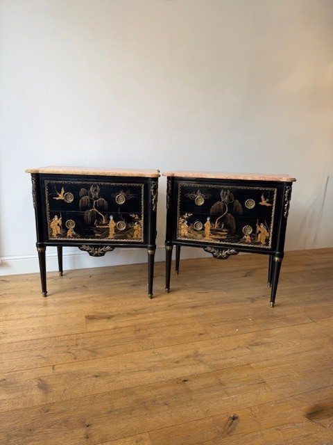 A pair of black lacquered Louis XVI style commodes featuring gold gilt Chinoiserie landscapes, marble tops, and tapered fluted legs.