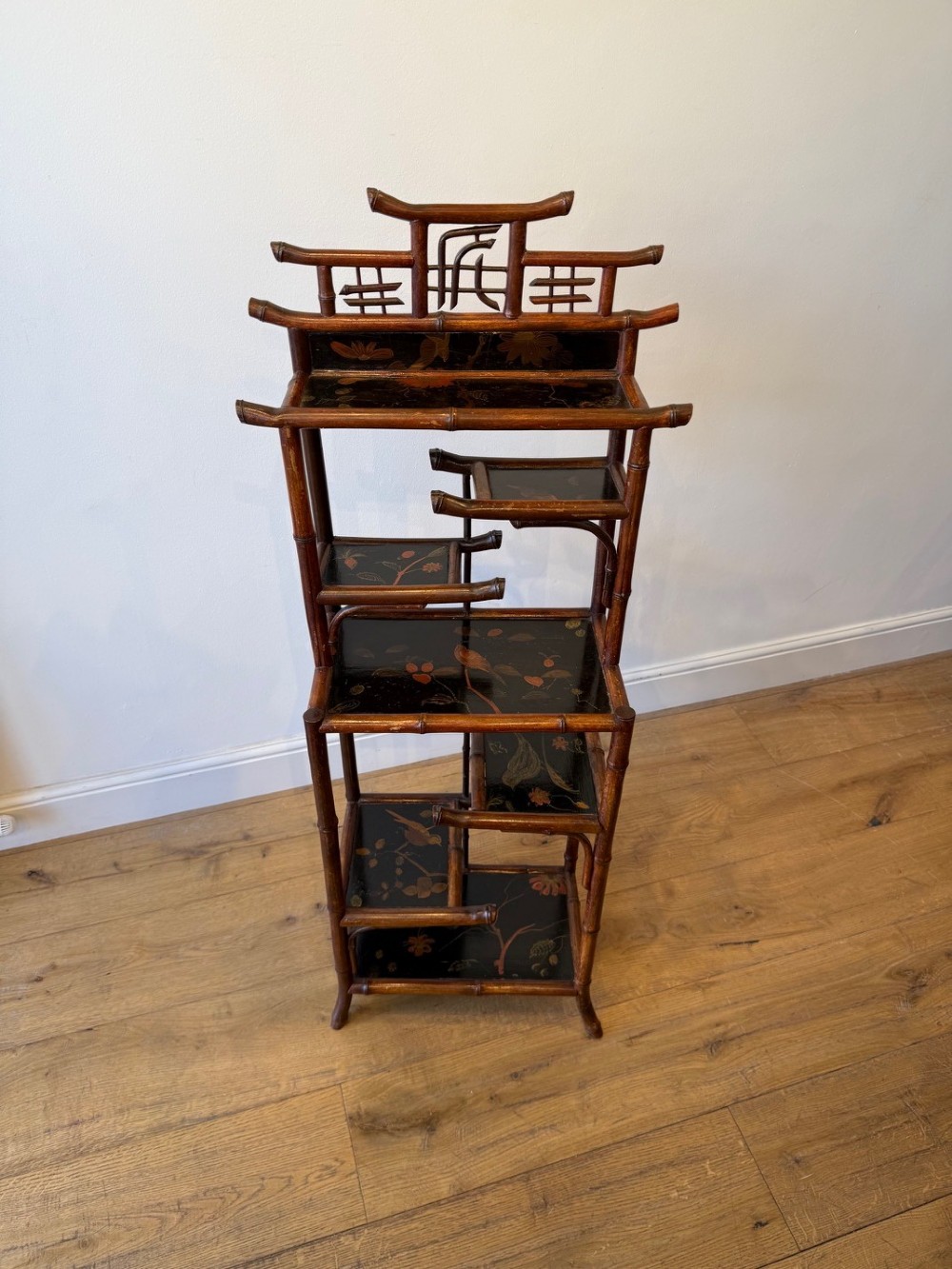 A dark bamboo tiered etagere display shelf with a pagoda-shaped top and black lacquer shelves painted with floral motifs.