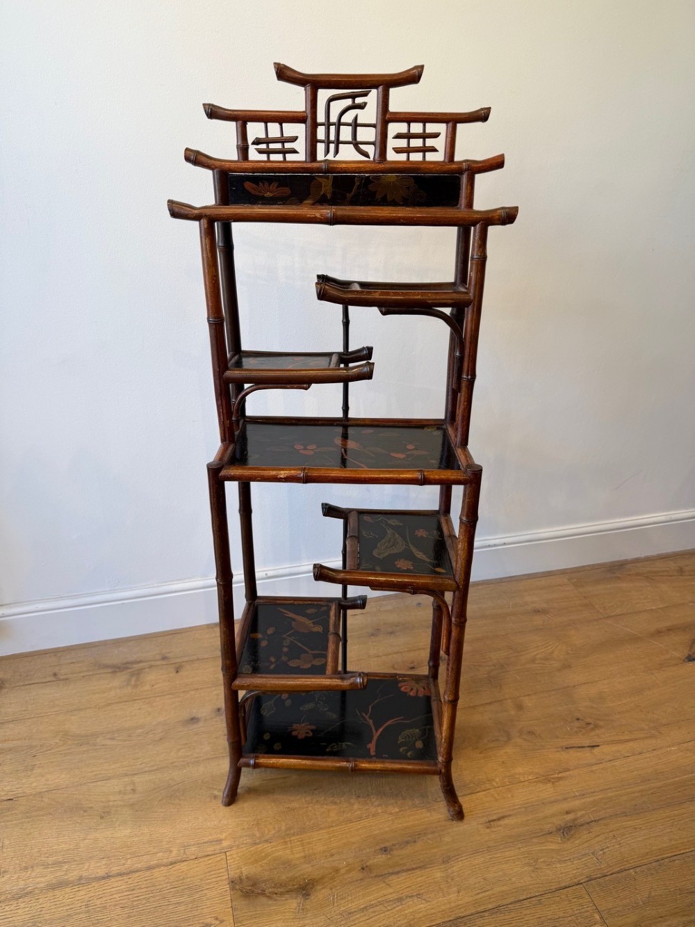 A dark bamboo tiered etagere display shelf with a pagoda-shaped top and black lacquer shelves painted with floral motifs. View II