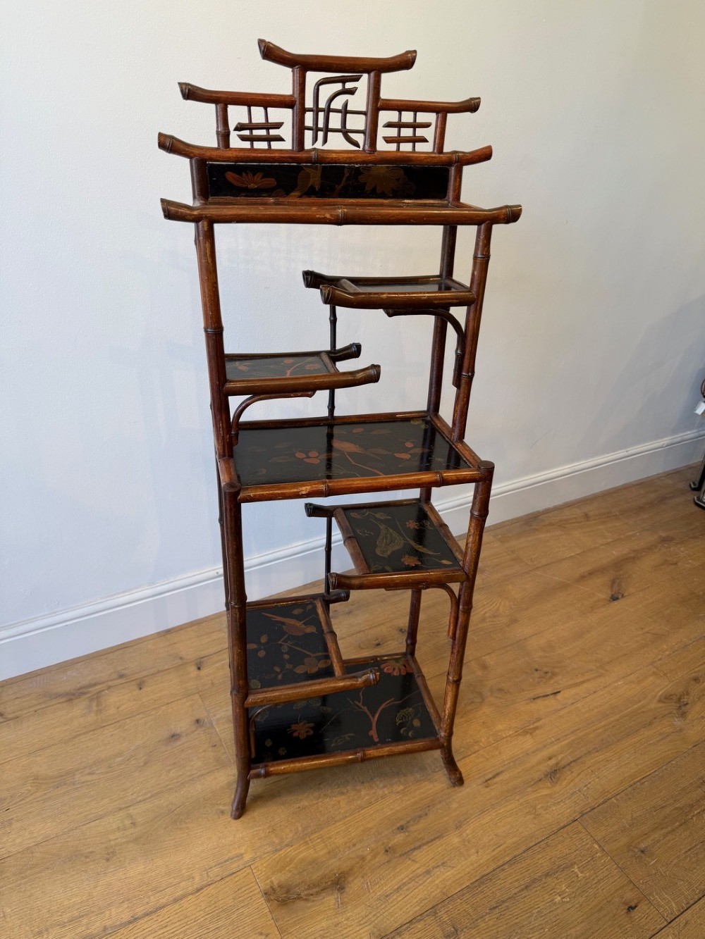 A dark bamboo tiered etagere display shelf with a pagoda-shaped top and black lacquer shelves painted with floral motifs. View III