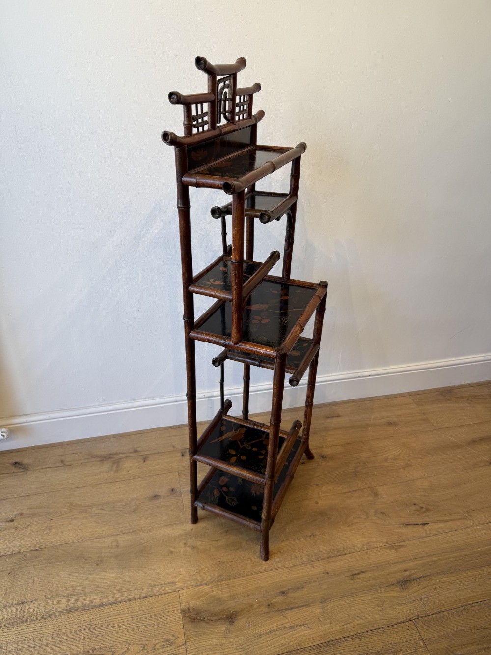 A dark bamboo tiered etagere display shelf with a pagoda-shaped top and black lacquer shelves painted with floral motifs. View VI