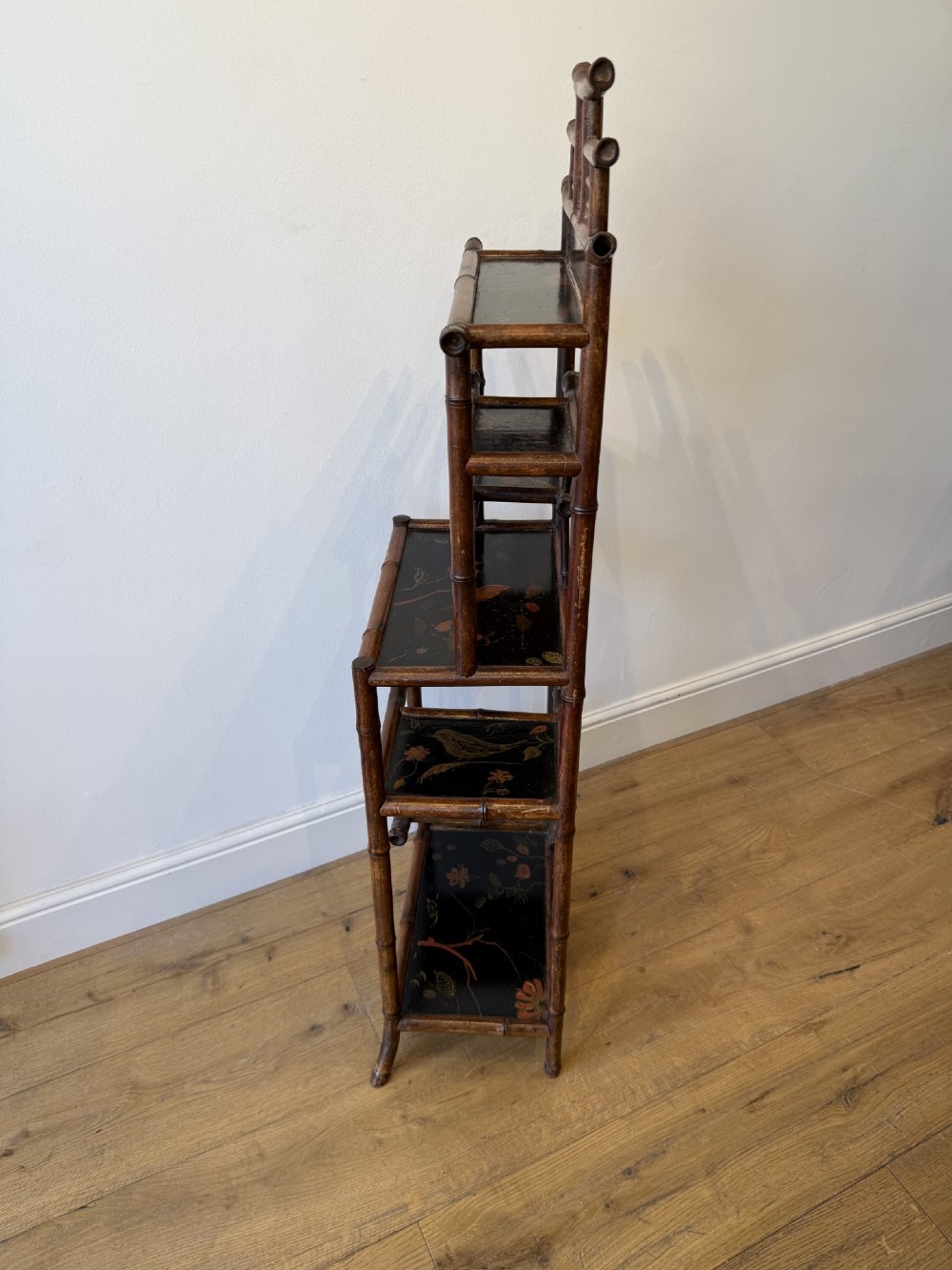 A dark bamboo tiered etagere display shelf with a pagoda-shaped top and black lacquer shelves painted with floral motifs. View VII