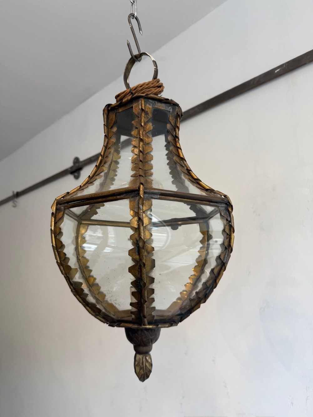 A vintage brass pendant lantern featuring curved glass panels framed with notched brass edging and a decorative bottom finial. View II