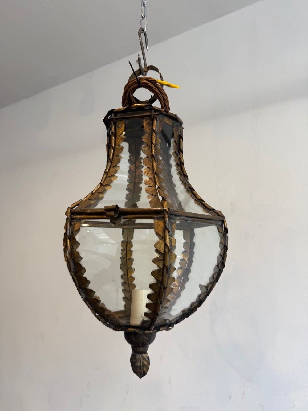 A vintage brass pendant lantern featuring curved glass panels framed with notched brass edging and a decorative bottom finial. View IV