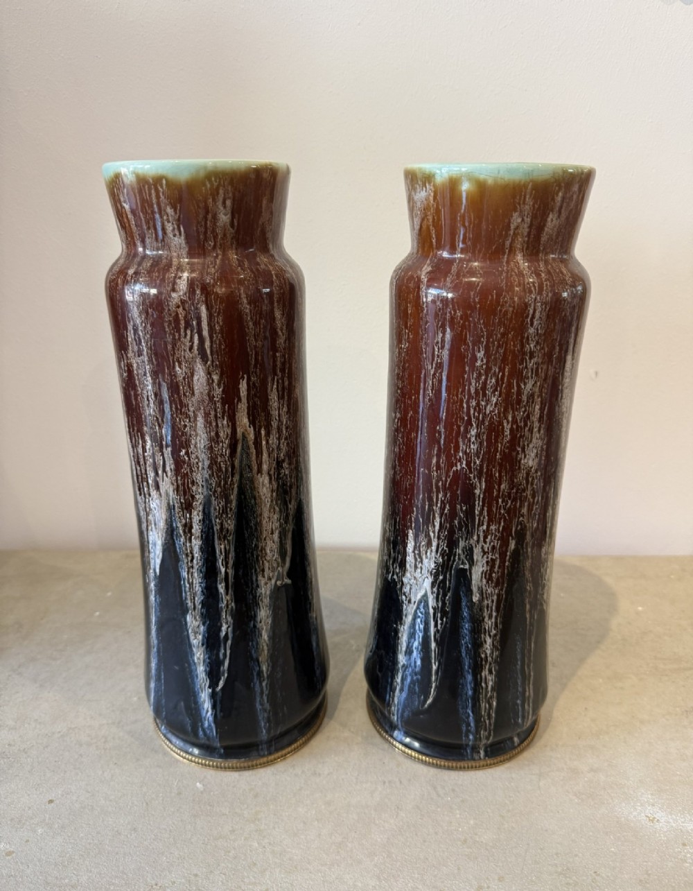 A pair of tall cylindrical antique ceramic vases featuring a dark brown and black drip glaze finish with brass mounts at the base.