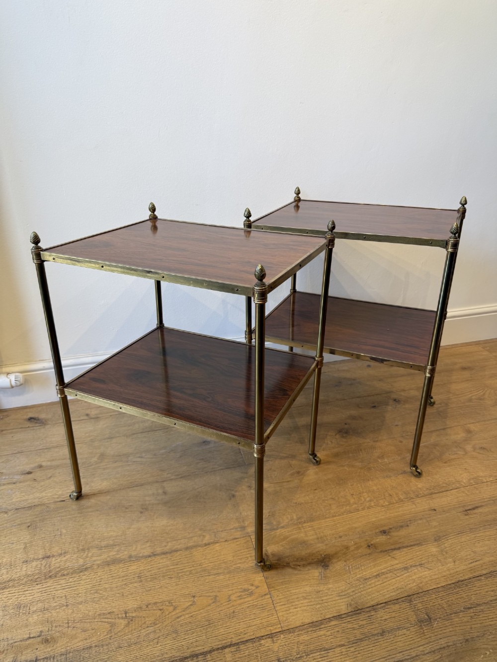 A pair of two-tier brass side tables featuring dark polished wood shelves, finial tops, and slender legs with small castors. View II