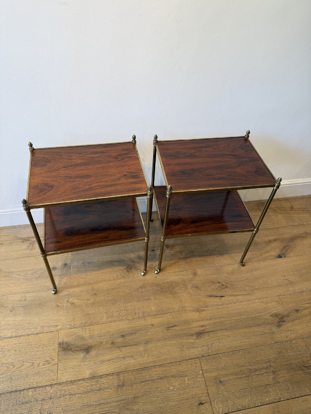 A pair of two-tier brass side tables featuring dark polished wood shelves, finial tops, and slender legs with small castors. View III
